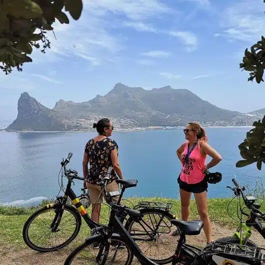 Two women with e-bikes at a viewpoint on Chapman’s Peak overlooking Hout Bay Two women with e-bikes at a viewpoint on Chapman’s Peak overlooking Hout Bay