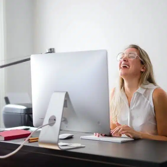 Woman laughing at her computer while taking part in a virtual team building event Woman laughing at her computer while taking part in a virtual team building event